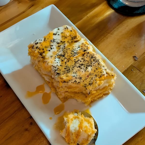 A partially eaten slice of layered cake with white frosting and orange drizzle, on a white plate.