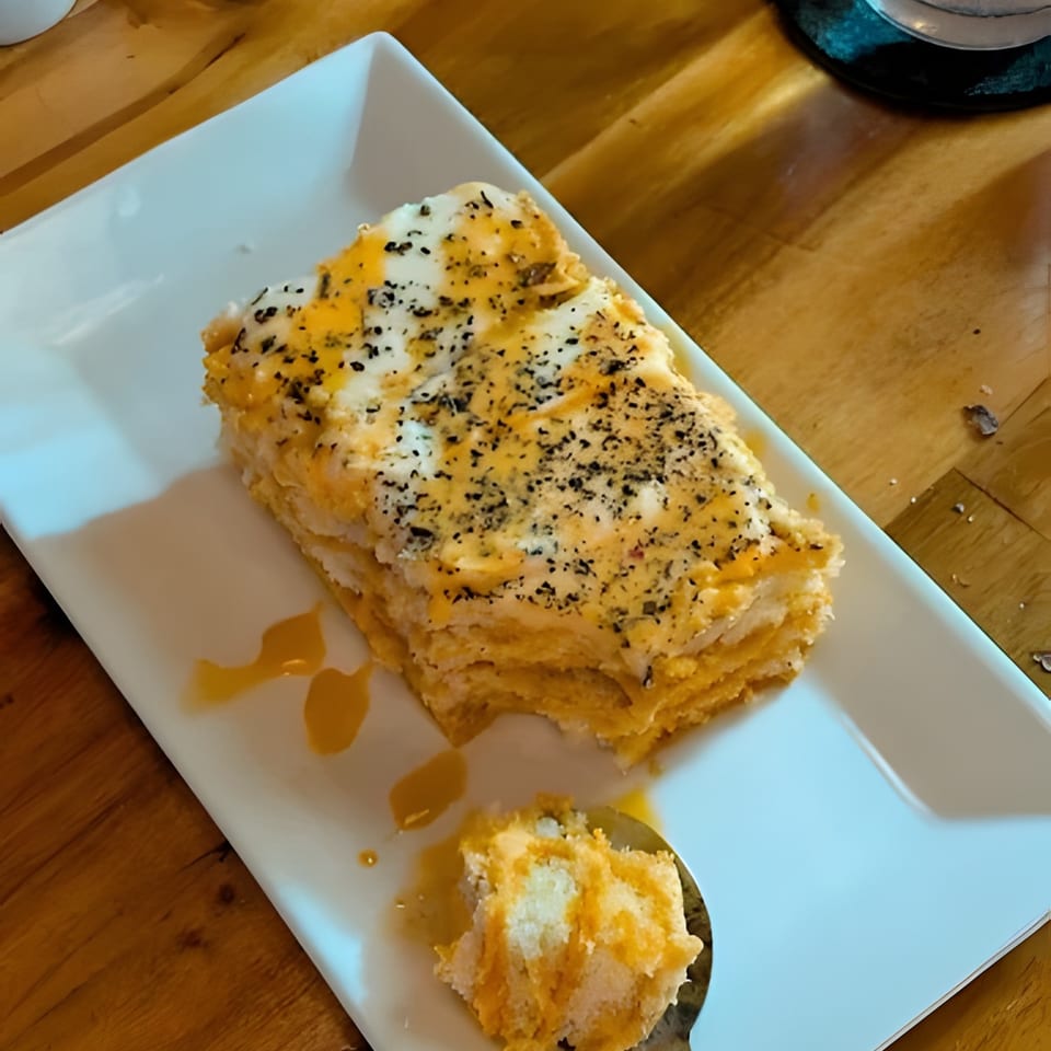 A partially eaten slice of layered cake with white frosting and orange drizzle, on a white plate.