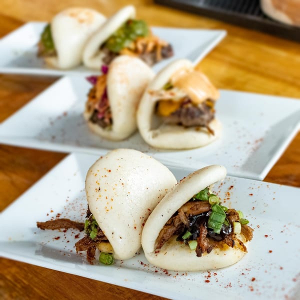 Three plates of bao buns with various fillings, including meat, green onions, and sauces.
