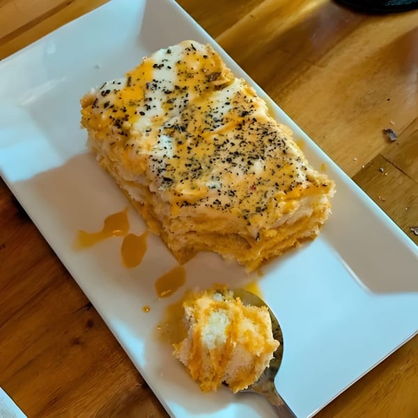A slice of layered dessert with white frosting and orange filling, topped with black specks.