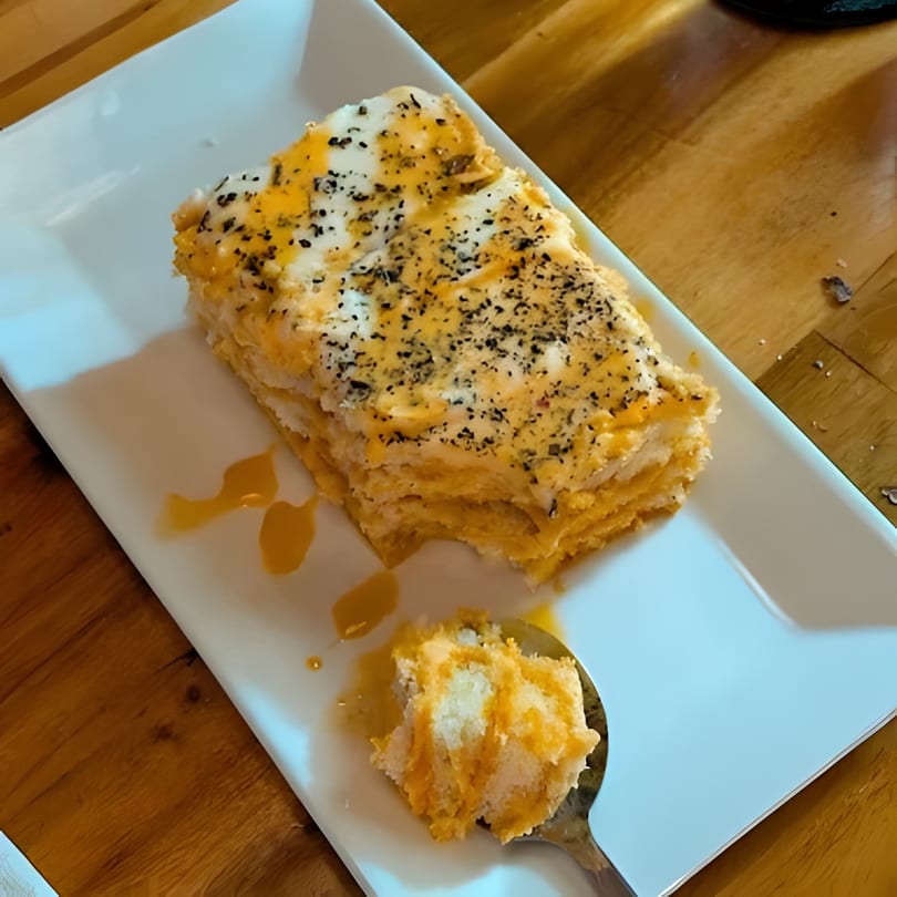 A slice of layered dessert with white frosting and orange filling, topped with black specks.