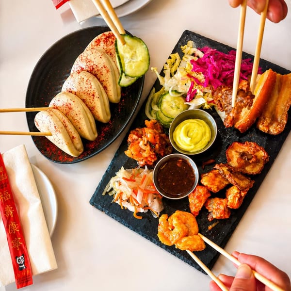 Overhead view of a shared platter with bao buns, pork belly, shrimp, and various sides.