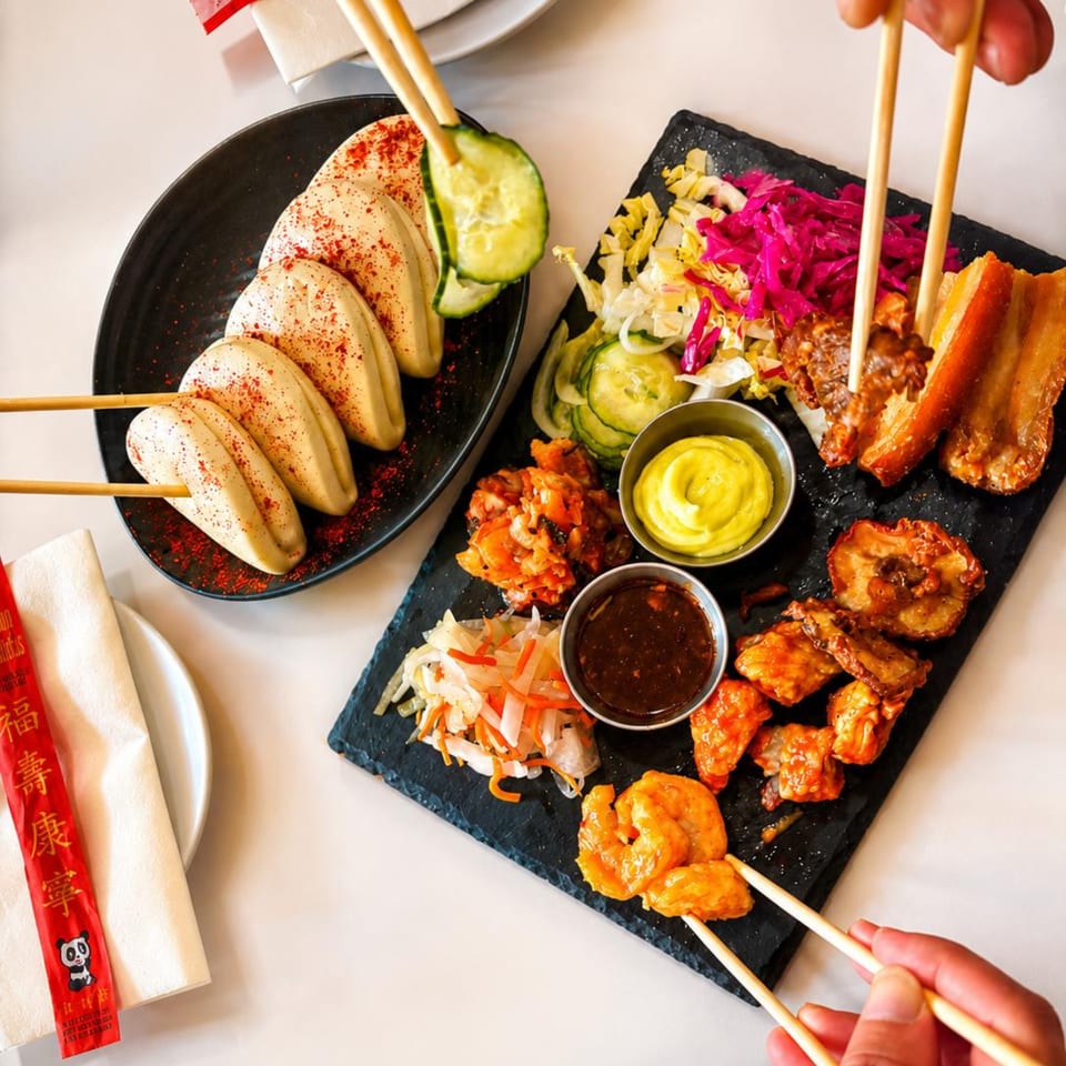 Overhead view of a shared platter with bao buns, pork belly, shrimp, and various sides.