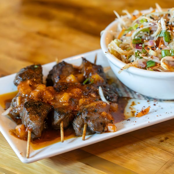 Grilled meat skewers with a sweet sauce and a side of coleslaw in a white bowl.